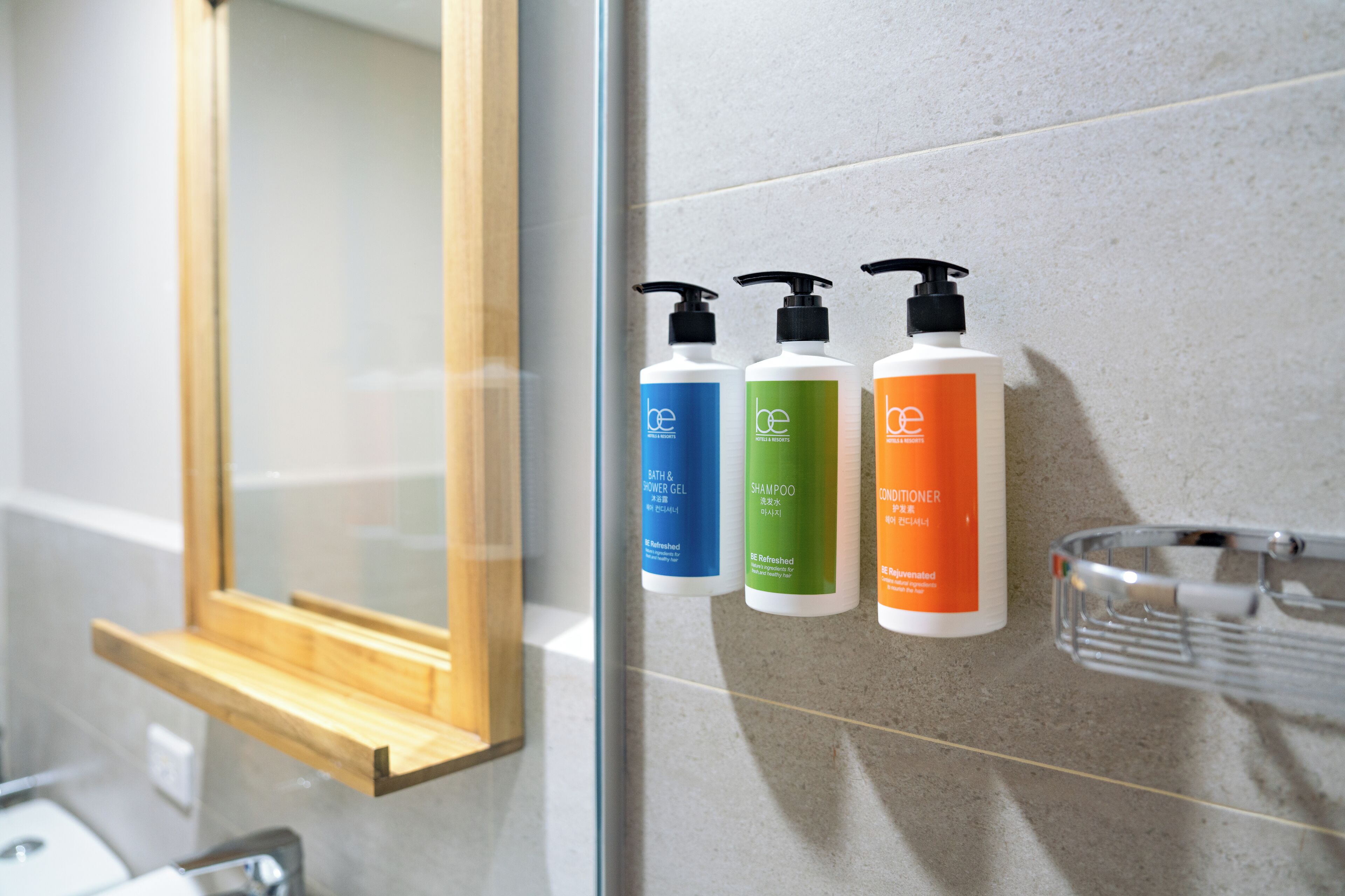 Une salle de bain avec un miroir, une étagère contenant trois flacons de produits de bain et un récipient en verre posé sur un porte-serviettes.