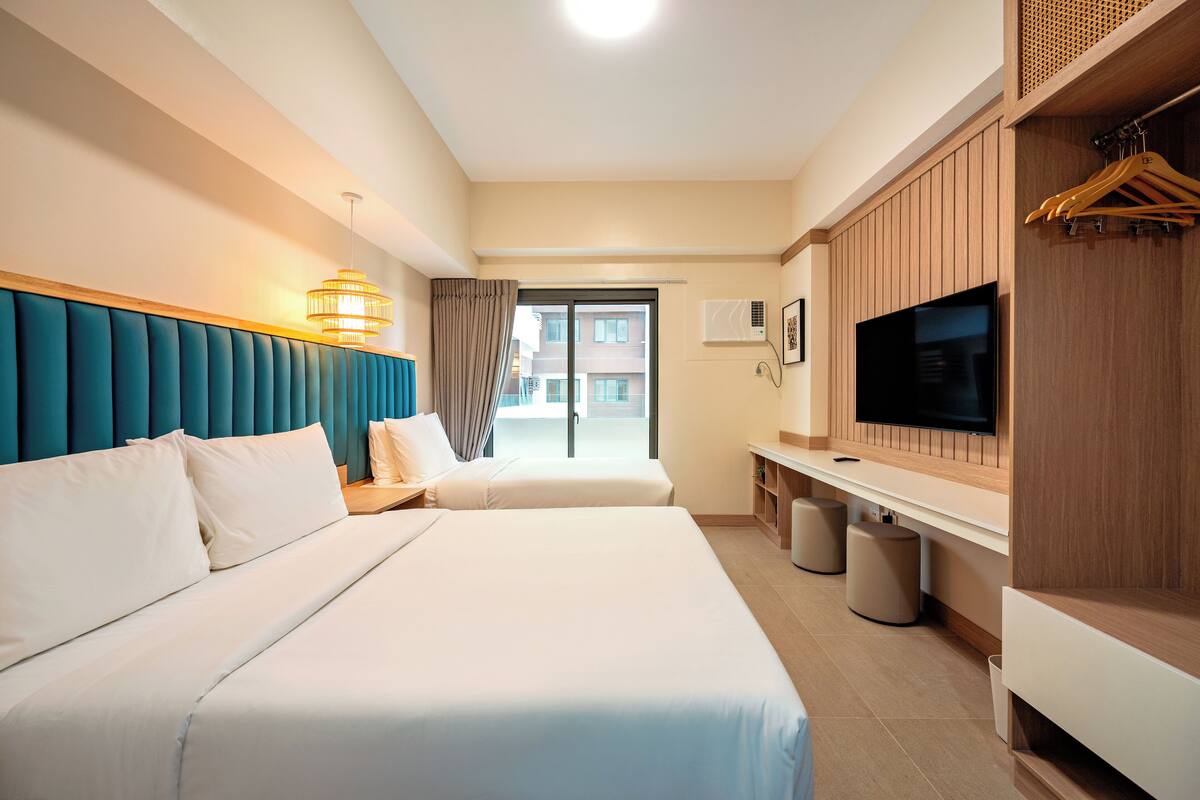 A hotel room with two beds, a TV, a wardrobe, and a balcony with a view.