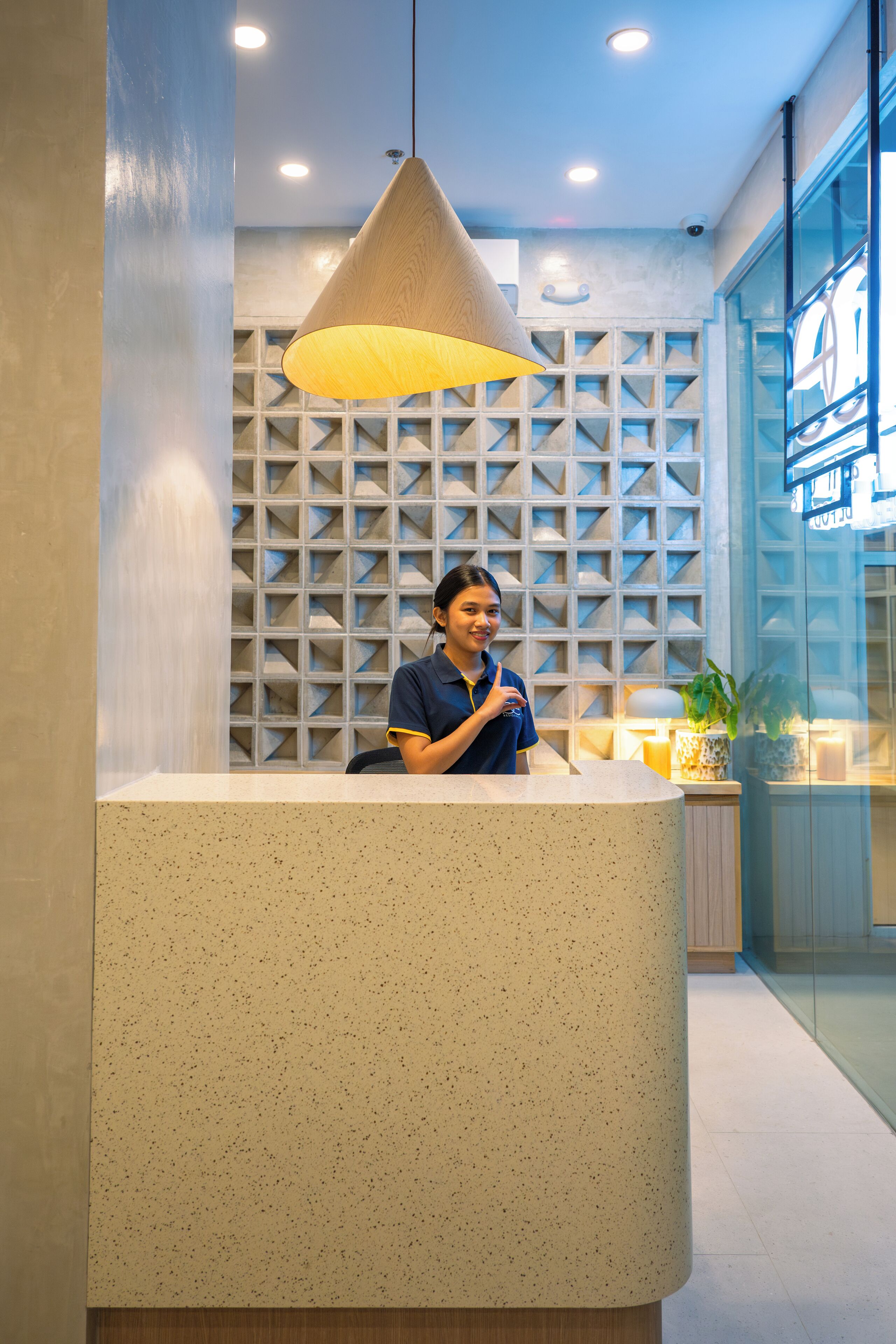 A reception desk with a modern design, a hanging pendant light, and a patterned wall in the background.