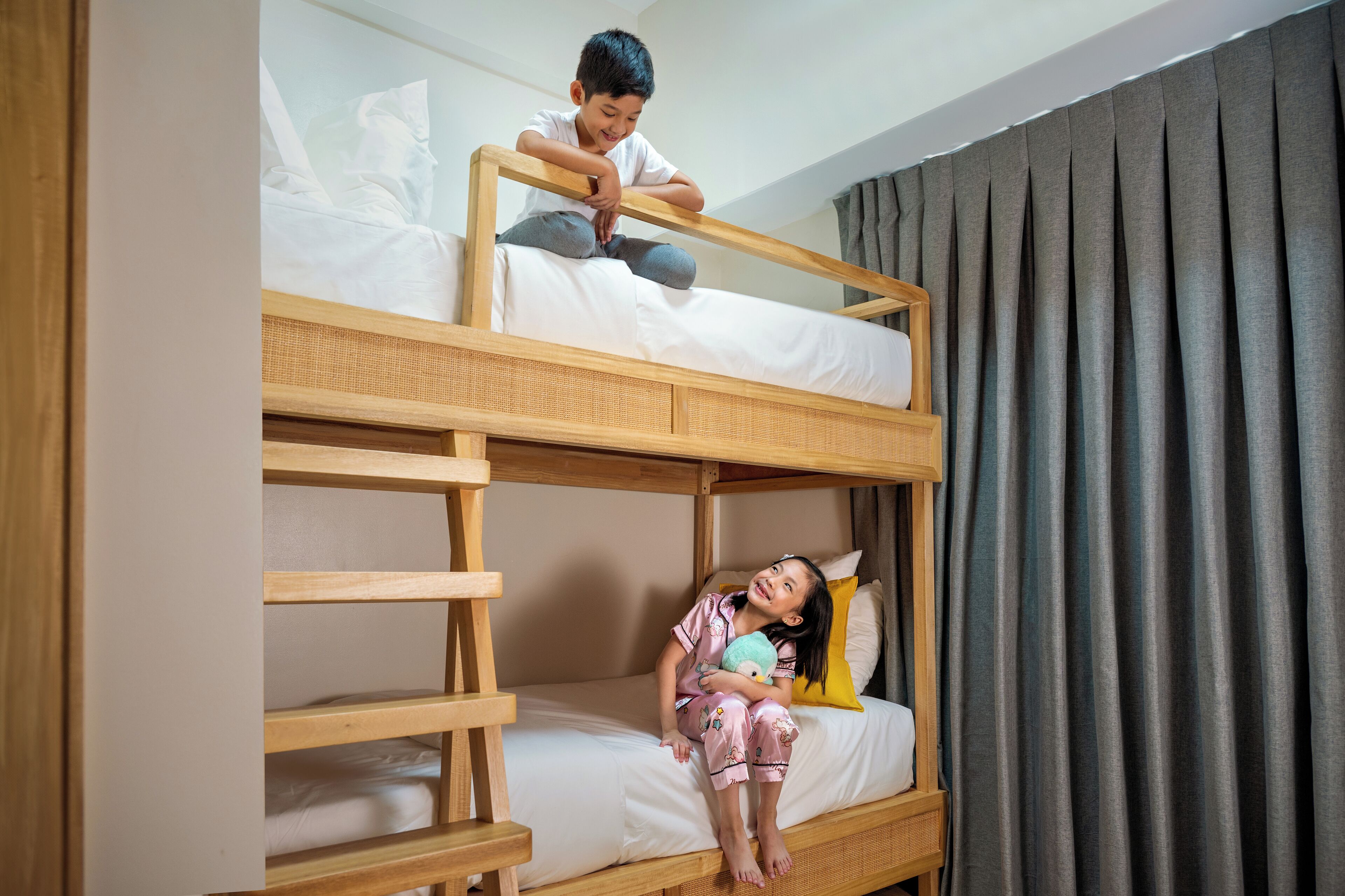 Un lit superposé avec un enfant assis sur le lit du bas et un autre enfant debout sur le lit du haut.