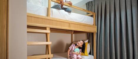 Una cama litera con un niño sentado en la cama inferior y otro niño de pie en la superior.