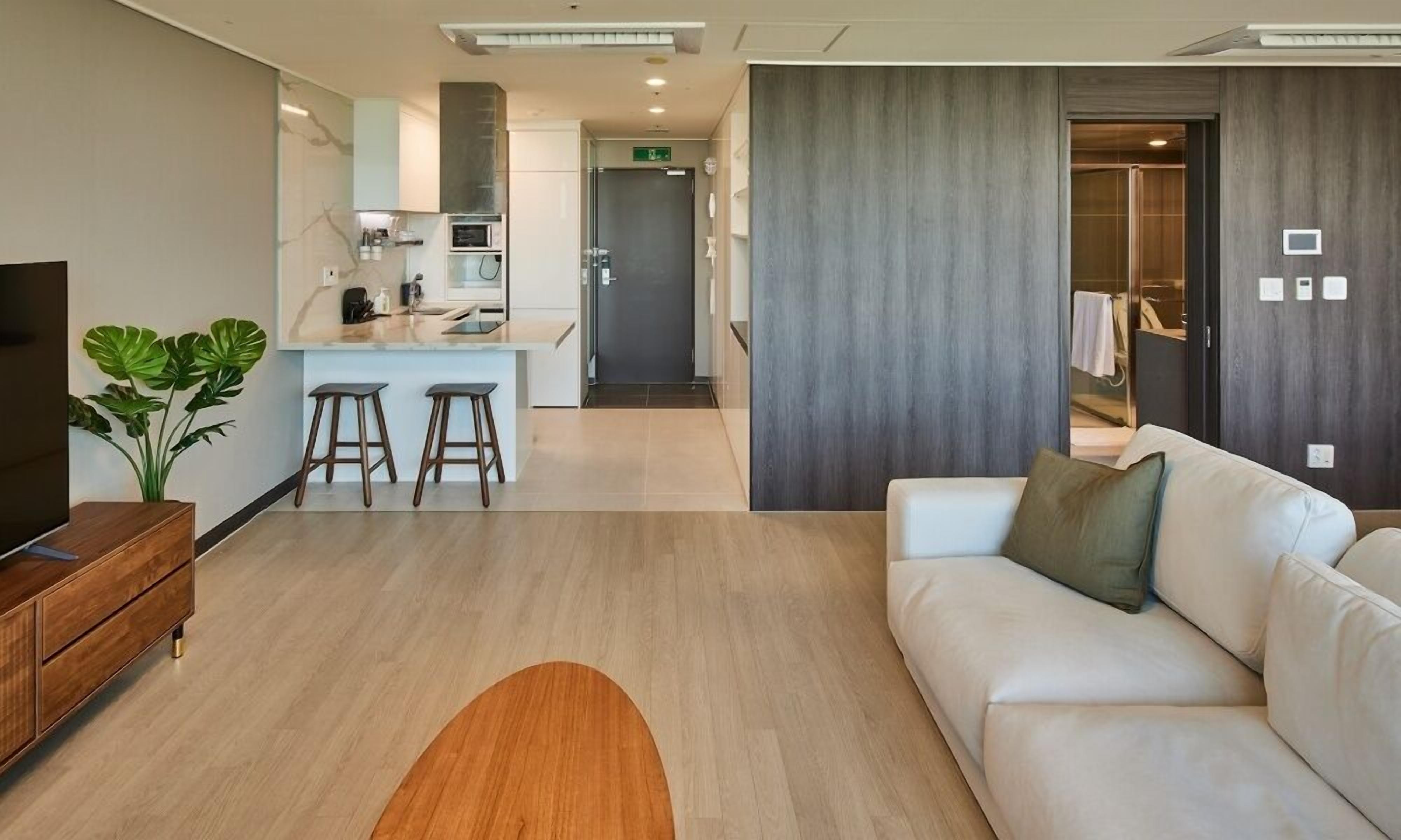 A modern hotel room with a sofa, a TV, a wooden side table, and a plant.