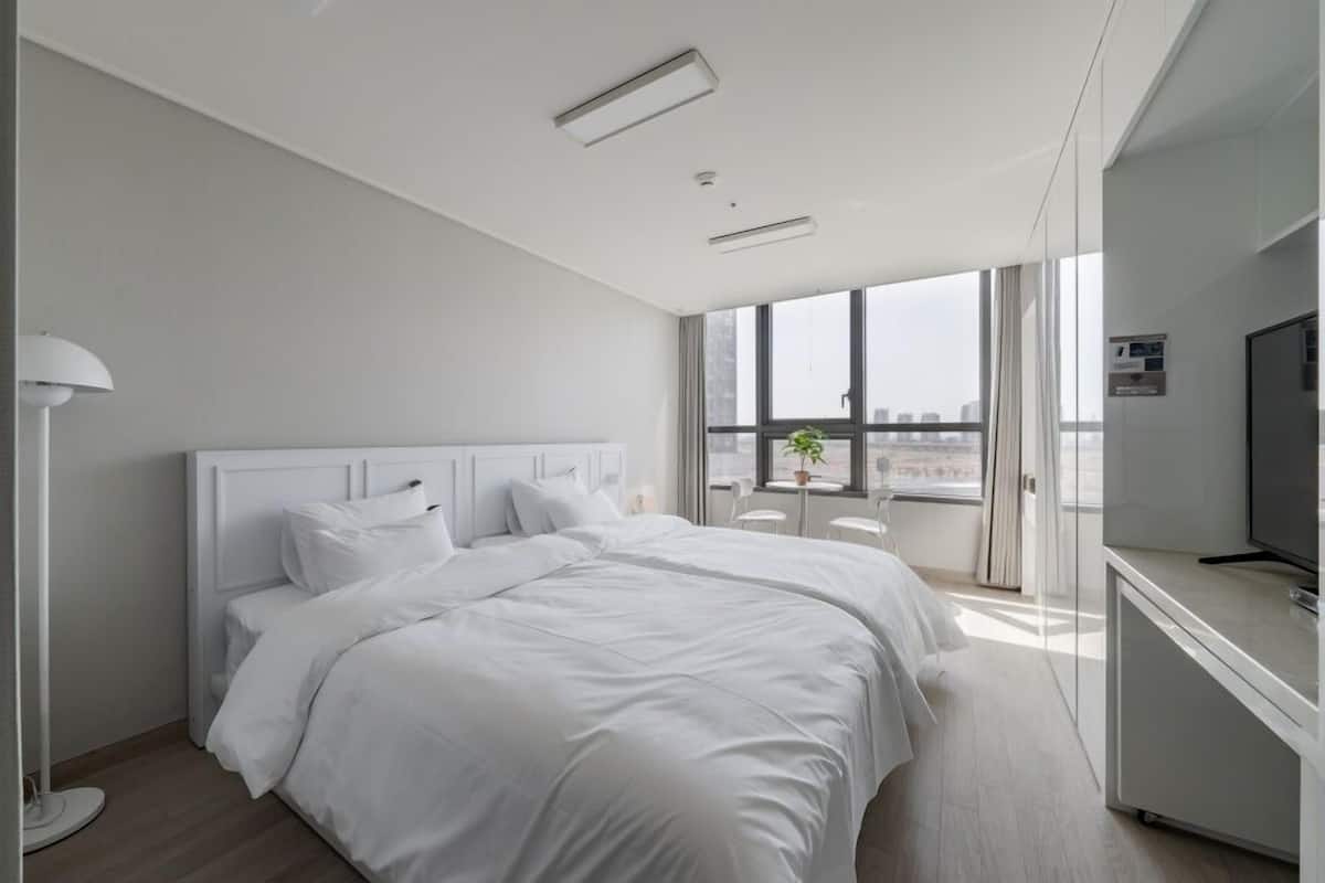 A modern hotel room with a large bed, a desk, a TV, and a window with a city view.