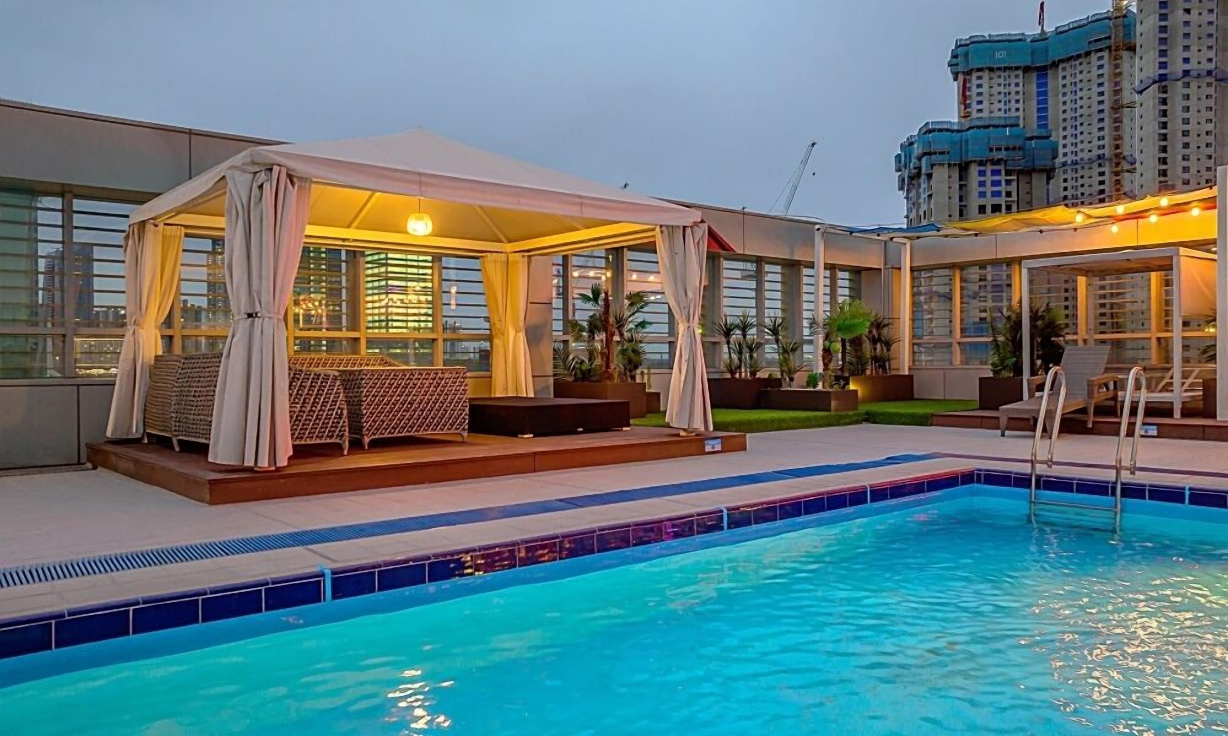 Uma área de piscina no terraço, com espaço coberto para sentar, piscina e vista para um edifício alto.