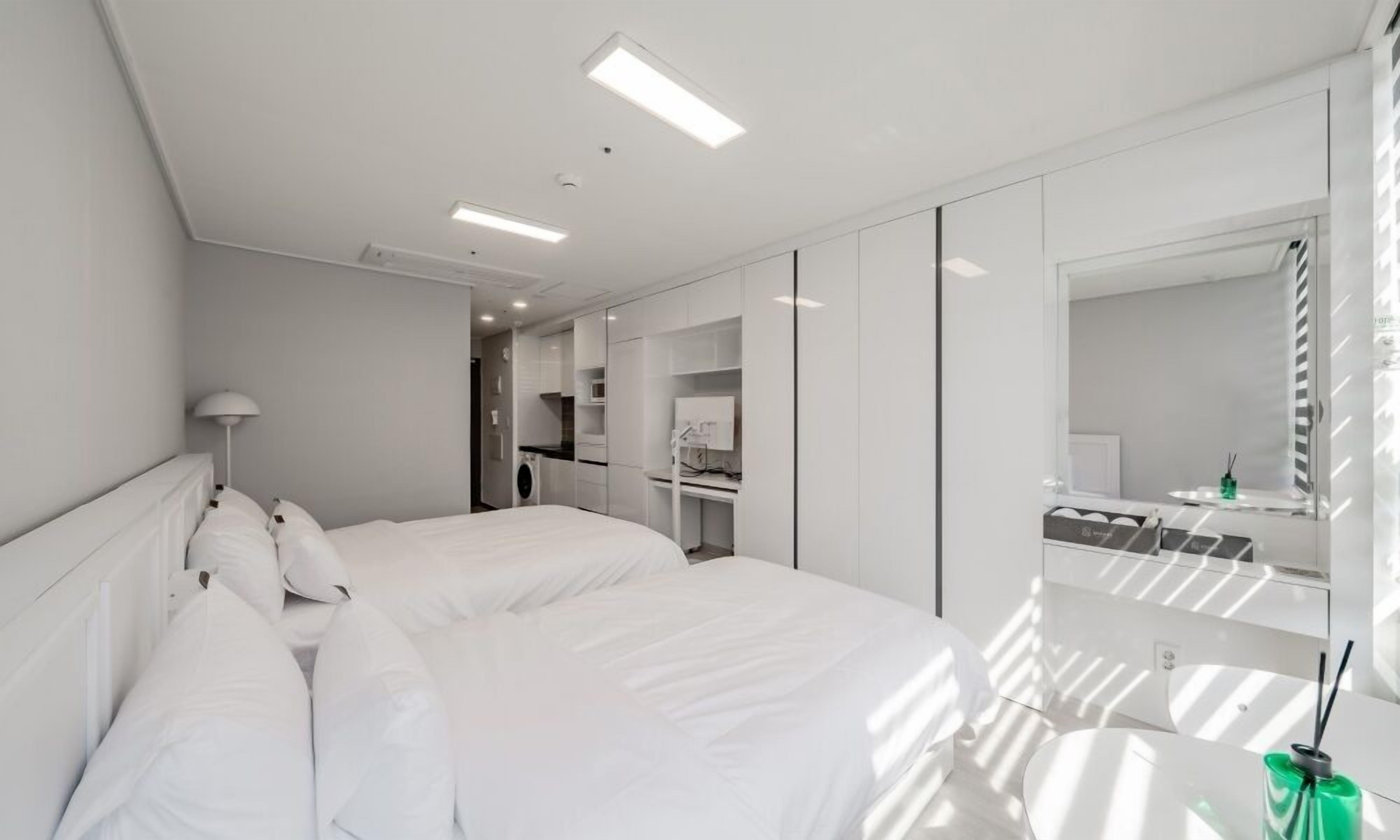 A modern hotel room with a large bed, a desk, a mirror, and a wardrobe.