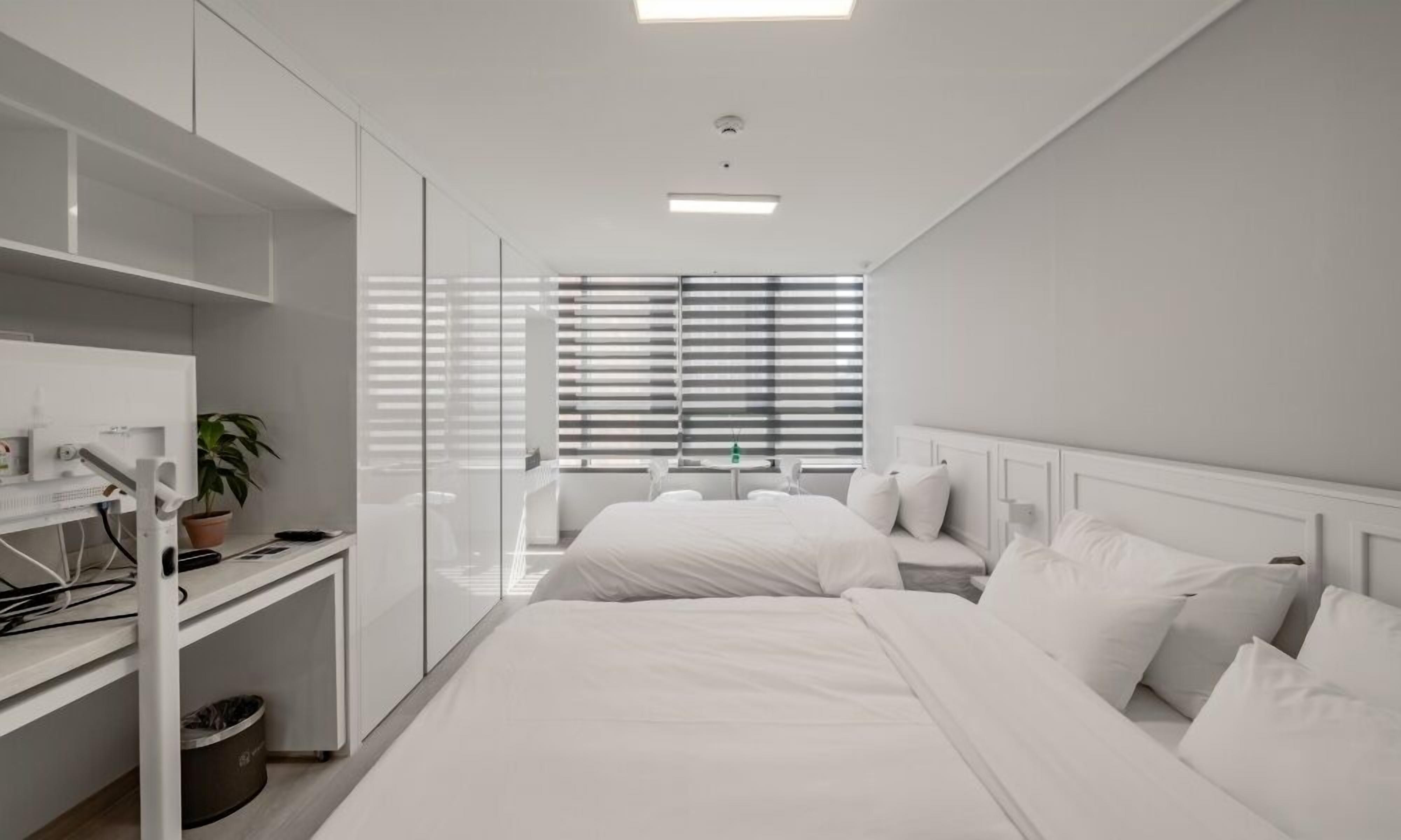 A modern bedroom with a bed, bedside tables, a desk, and a window with blinds.