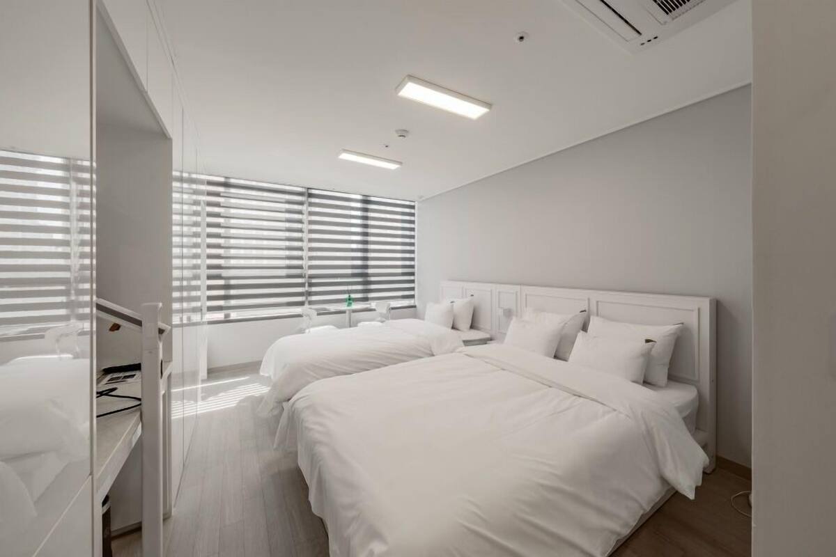A hotel room with two beds, a desk, and a window with blinds.