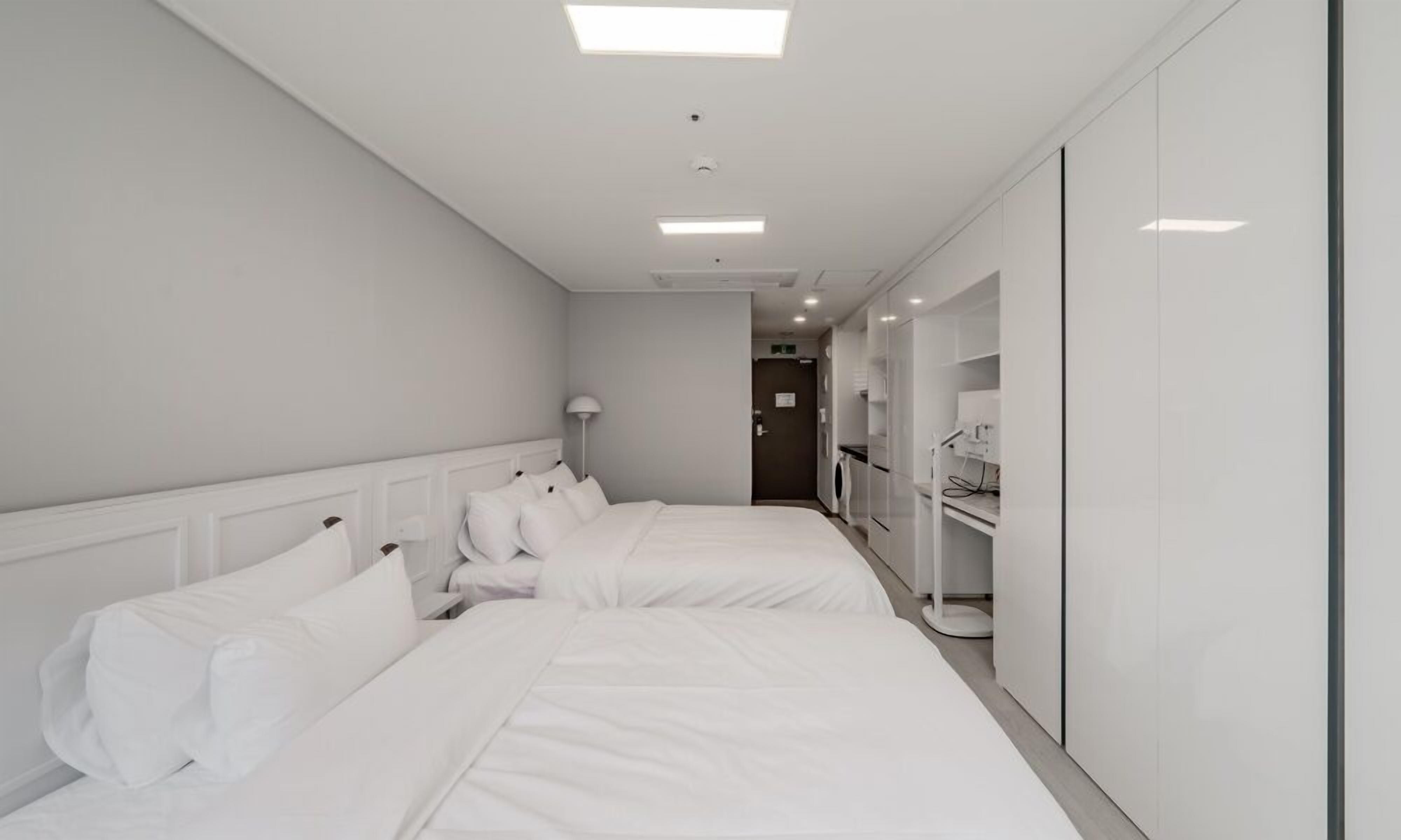 A hotel room with two beds, a bedside table, a lamp, and a wardrobe.