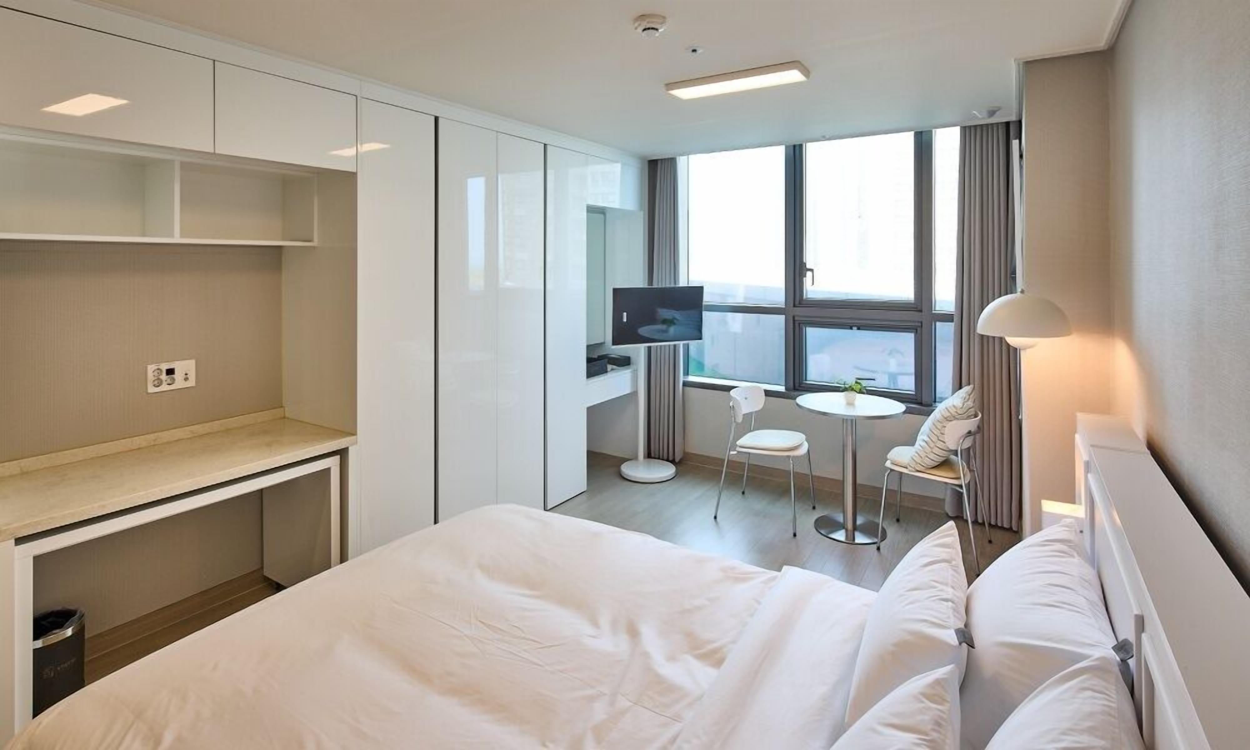 Habitación de hotel moderna con una cama grande, un escritorio, un televisor y una pequeña mesa con sillas.