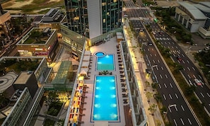 Une piscine sur le toit, dotée de deux espaces de baignade distincts, entourée de chaises longues et protégée par une paroi en verre.