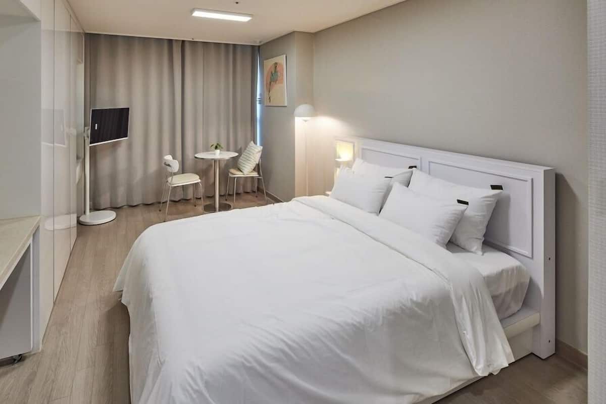 A modern hotel room with a large bed, a desk, a chair, and a small table.