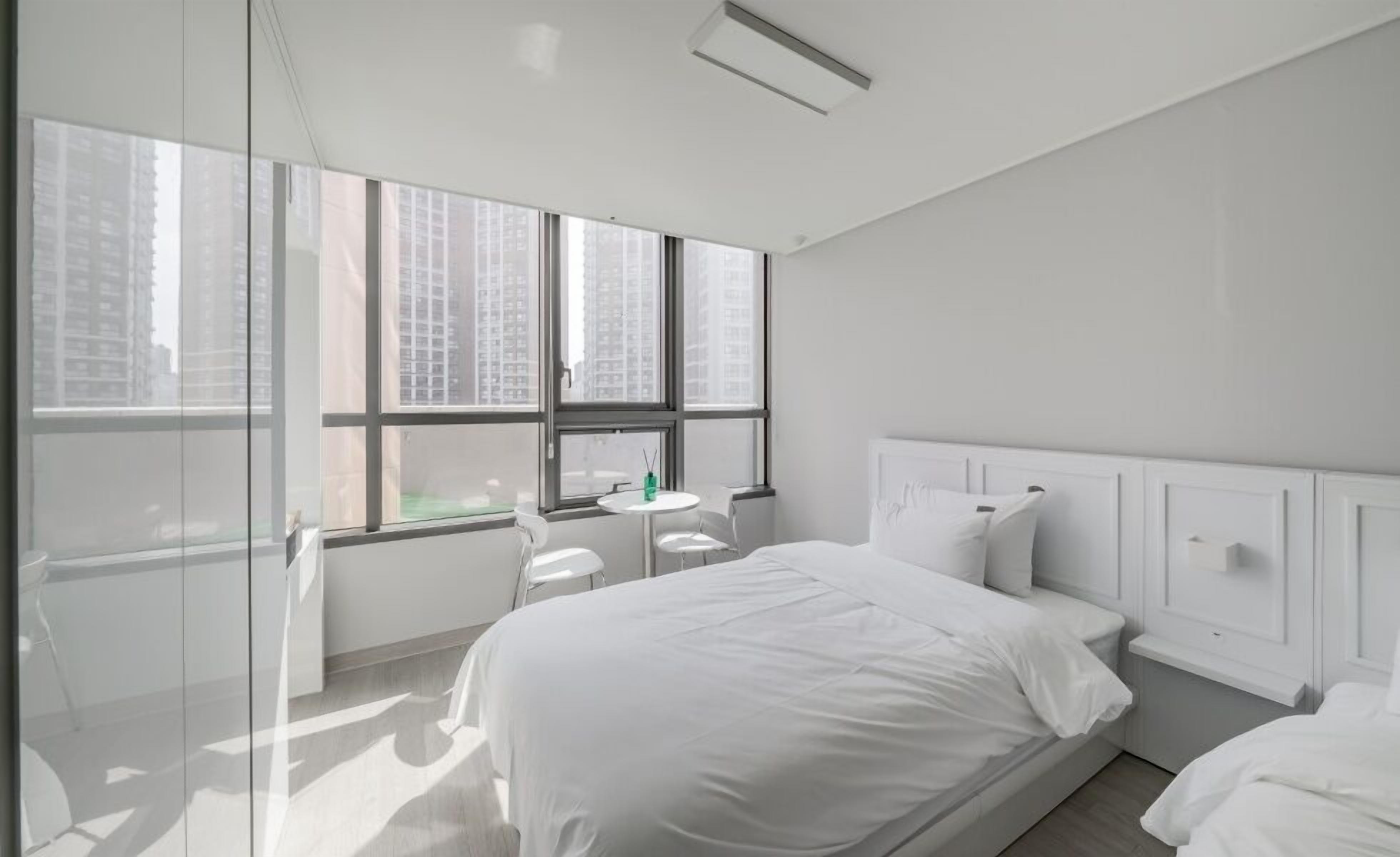 A modern hotel room with a large window, a bed, a small table, and a chair.