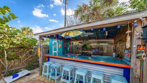 A beachside bar with a blue and orange color scheme, outdoor seating, and a sign advertising 'Tiki in the Wild'.