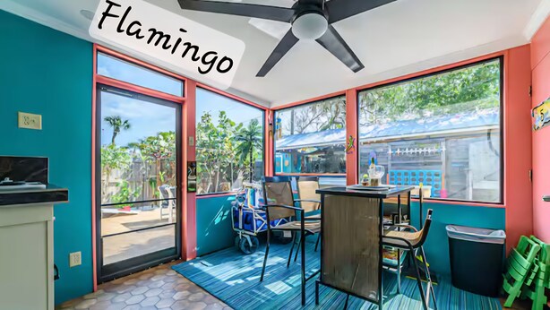 A room with teal walls, a large window, a ceiling fan, and a table with chairs.