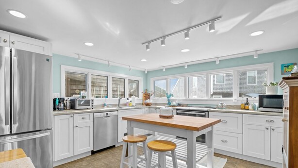 Una cocina moderna con armarios blancos, electrodomésticos de acero inoxidable y una isla de madera con taburetes.