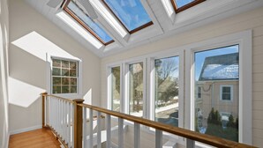 Una escalera con barandillas de madera que conduce a una habitación con tragaluces y ventanas amplias.