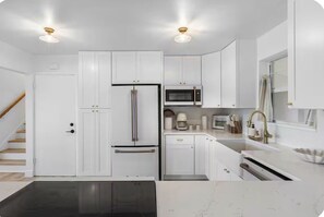 A modern kitchen with white cabinetry, a stainless steel refrigerator, a microwave, and a black countertop.