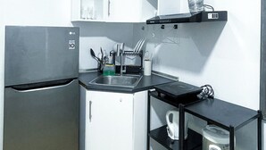 A compact kitchen with a refrigerator, a sink, a dishwasher, and a black countertop with shelves. - Room-warm Urban Studio With Modern Desig (Iloilo)