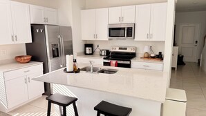 Une cuisine moderne avec des meubles blancs, des appareils en acier inoxydable, un plan de travail en marbre et un îlot central doté de tabourets.