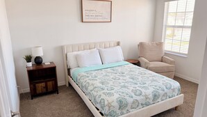 Une chambre à coucher avec un lit, une chaise, une table de chevet, une lampe et une citation encadrée accrochée au mur.