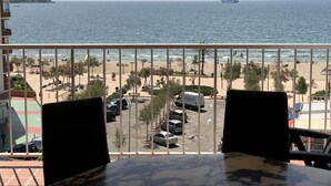 A balcony with a view of a beach, a ship in the distance, and parked cars. - Apartment in Roses in first sea line (Roses)