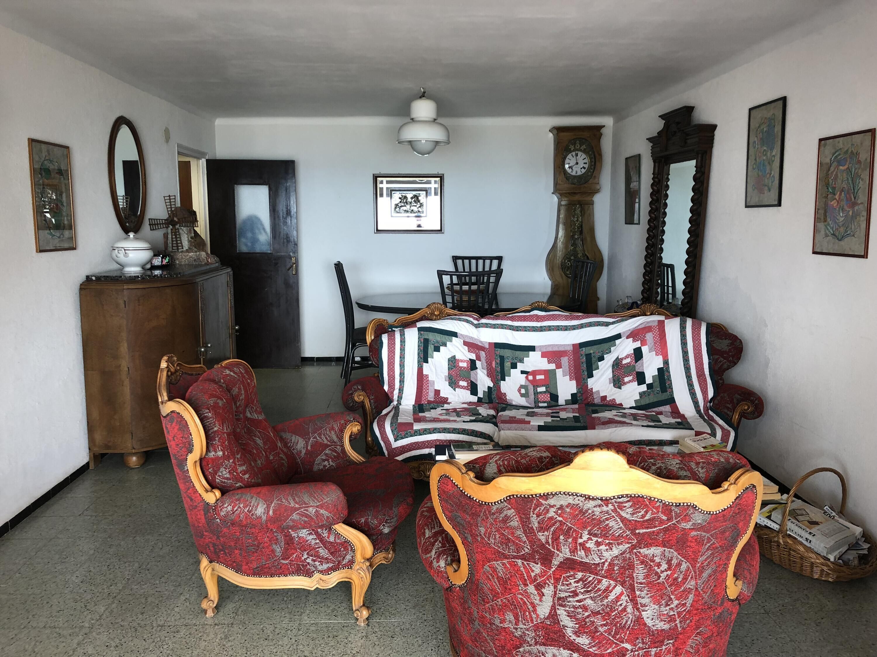 A room with a vintage red and gold armchair, a wooden cabinet, a large clock, and a framed picture on the wall.