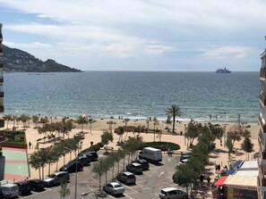 A coastal cityscape with a beach, parked cars, and a large ship in the distance. - Apartment in Roses in first sea line (Roses)