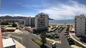 A coastal residential area with a parking lot, a road with a pedestrian crossing, and buildings with balconies overlooking the beach. - Apartment in Roses in first sea line (Roses)