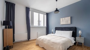 Et soveværelse med seng, sengeborde, gulvlampe, radiator og et vindue med gardiner.