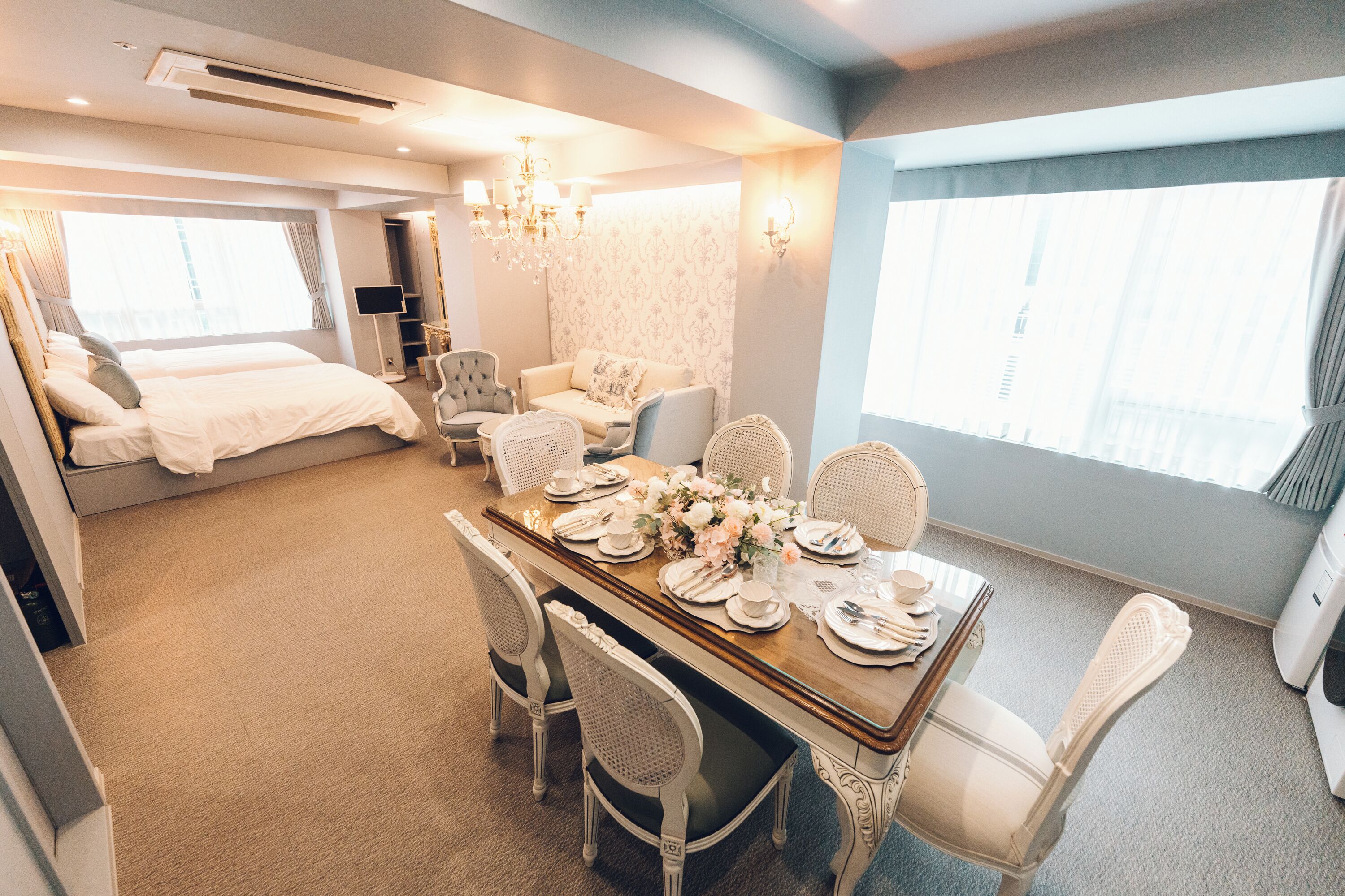 A hotel room with a dining area, a bed, a sofa, and a TV.