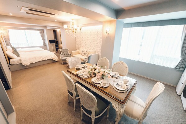 A hotel room with a dining area, a bed, a sofa, and a TV.