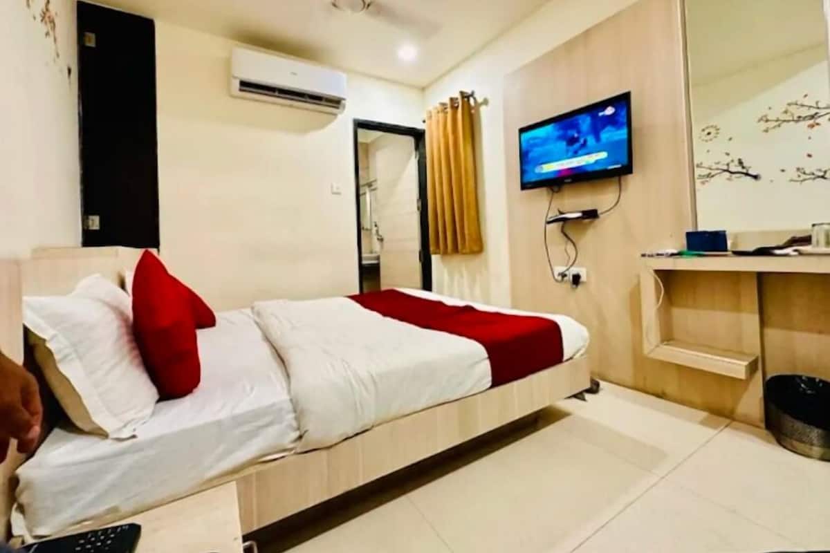 A hotel room with a bed, a television, an air conditioning unit, and a bathroom visible through an open door.