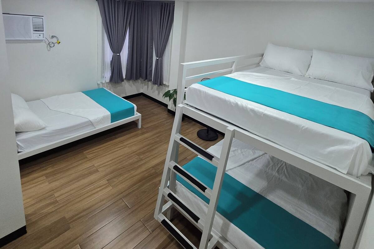 Ein Hotelzimmer mit zwei Etagenbetten, einem kleinen Tisch, einem Stuhl, einer Zimmerpflanze und einem Fenster mit Vorhängen.