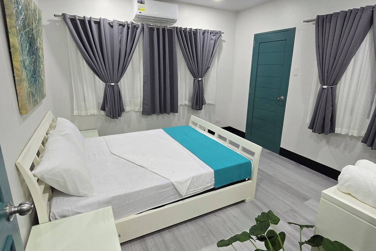 Ein modernes Schlafzimmer mit einem Bett, Vorhängen, einem Blumentopf und einer Tür.