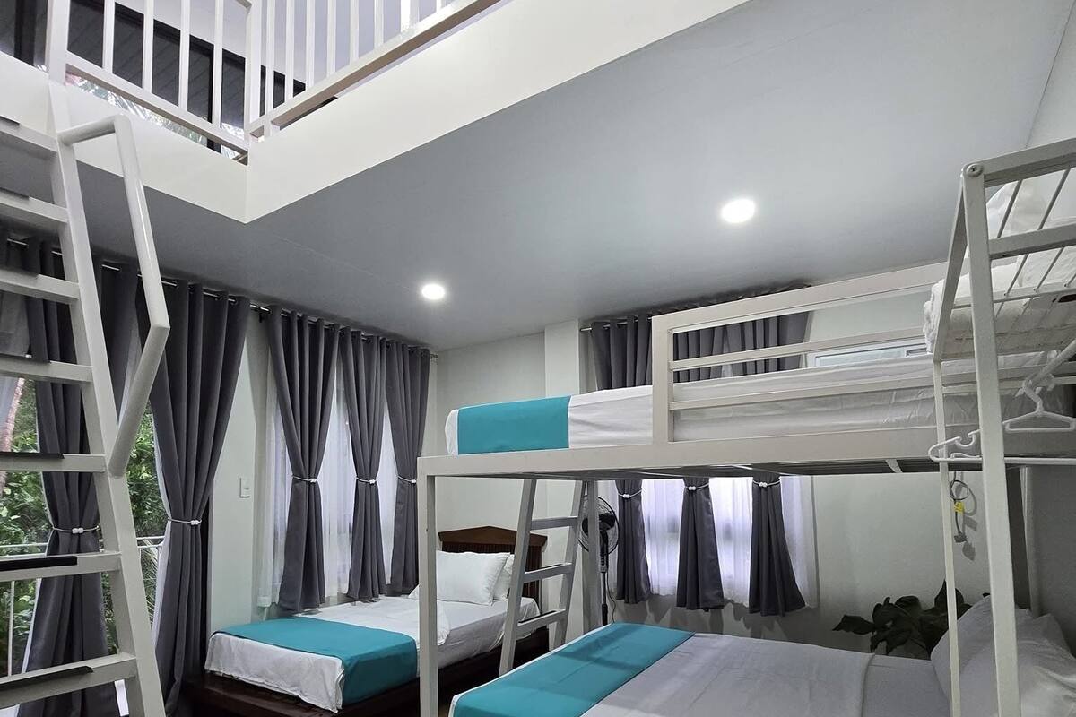 Ein Schlafsaalzimmer mit Etagenbetten, Holzboden und einem Balkon mit Geländer.