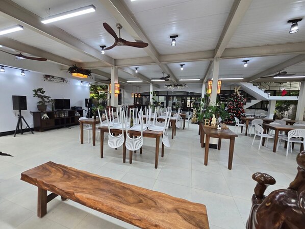 Un grand espace intérieur comprenant plusieurs tables et chaises, des ventilateurs de plafond et un sapin de Noël.