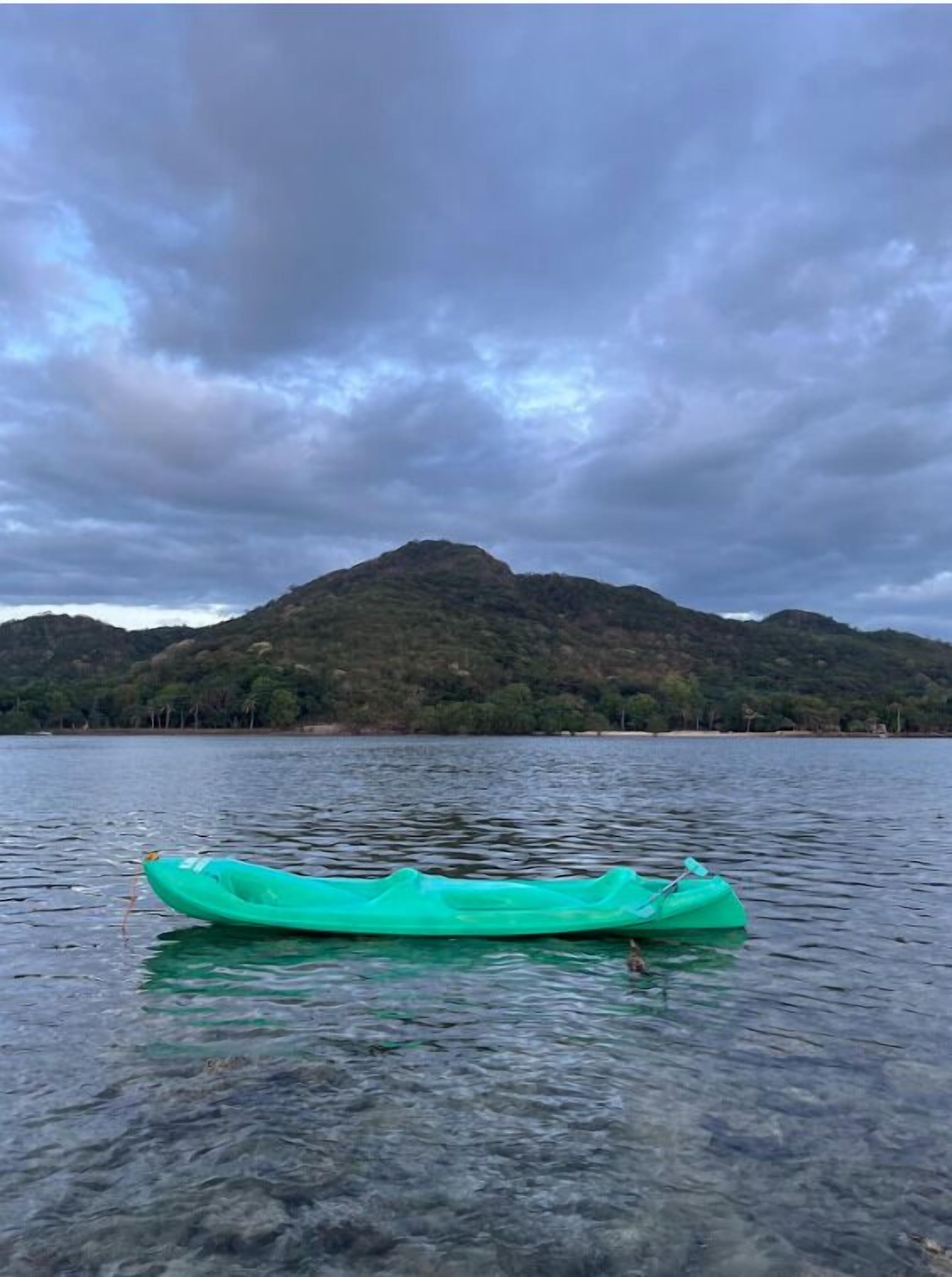 Un kayak verde sobre aguas tranquilas, con una montaña al fondo.