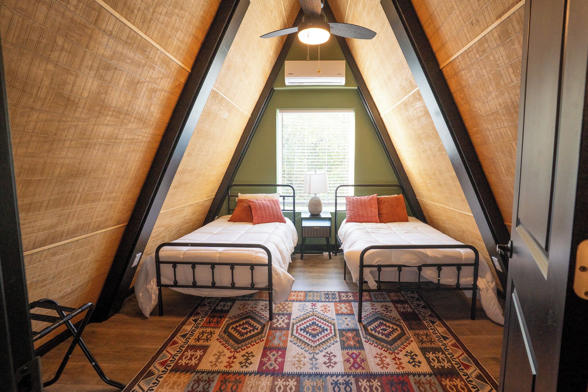 A triangular attic bedroom with two beds, a patterned rug, and a ceiling fan.
