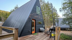 A modern, triangular wooden cabin with a deck and outdoor seating area. - Golf Lovers 2-bedroom A-Frame Cabin by Big Cedar Golf (Omaha)