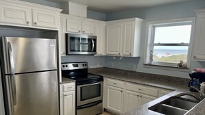 A kitchen with white cabinets, stainless steel appliances, granite countertops, and a window with a view. - Beachgate Condo Suites And Hotel 521+522a+522b 3 Bedroom Condo (Port Aransas)