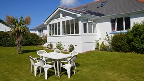 Une maison blanche avec un patio couvert, une pelouse avec une table et des chaises, et un palmier.