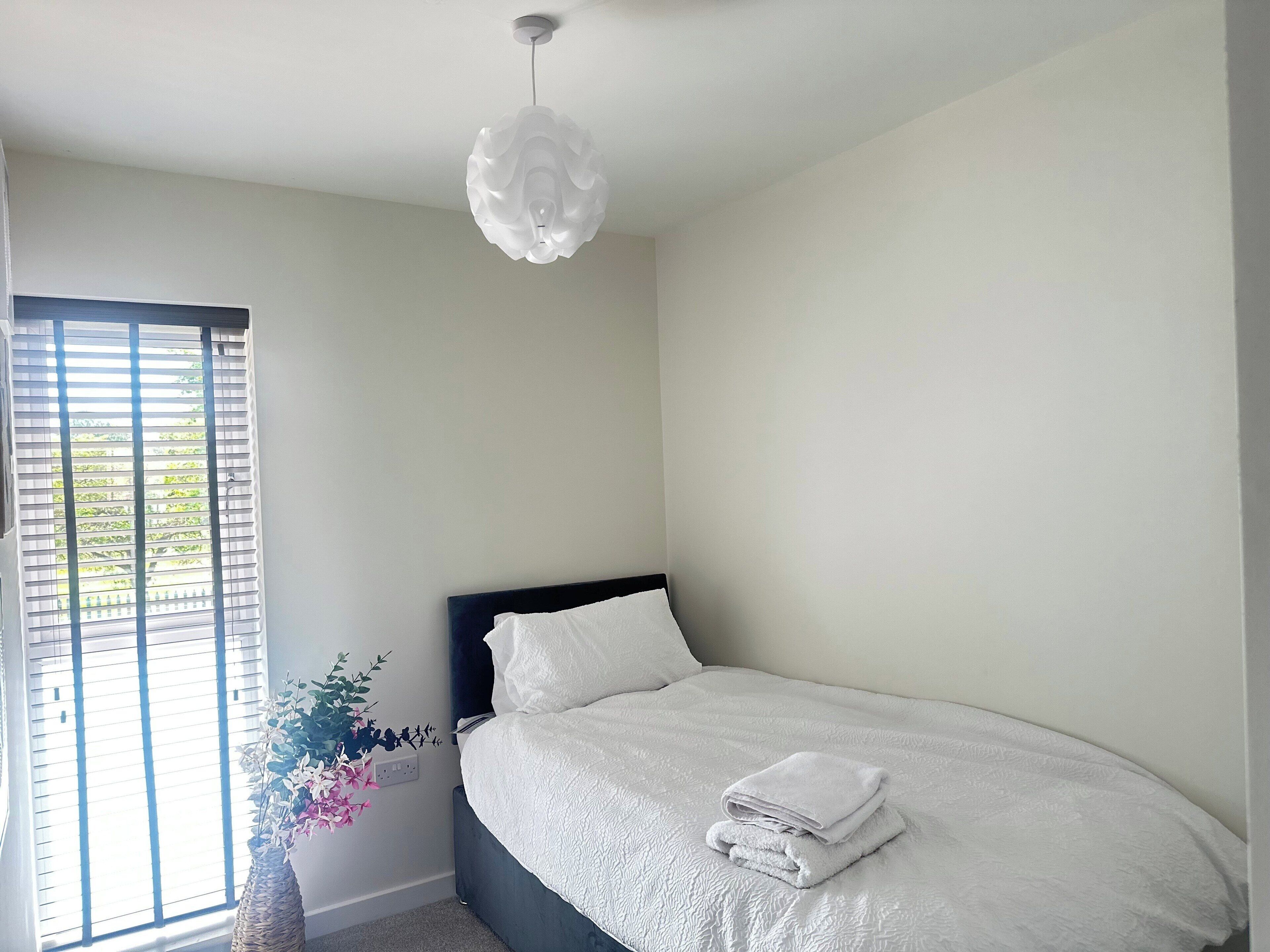 Een slaapkamer met een bed, een raam met zonwering en een hanglamp.