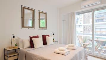 Quarto de hotel com uma cama, duas mesas de cabeceira, um abajur, uma planta em vaso e vista para a varanda externa.