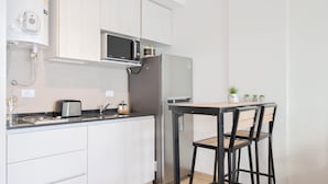 Eine moderne Küche mit weißen Schränken, einem Edelstahl-Kühlschrank, einer Mikrowelle und einem Toaster. Ein kleiner Tisch mit Stühlen und ein Blumentopf sind ebenfalls vorhanden.