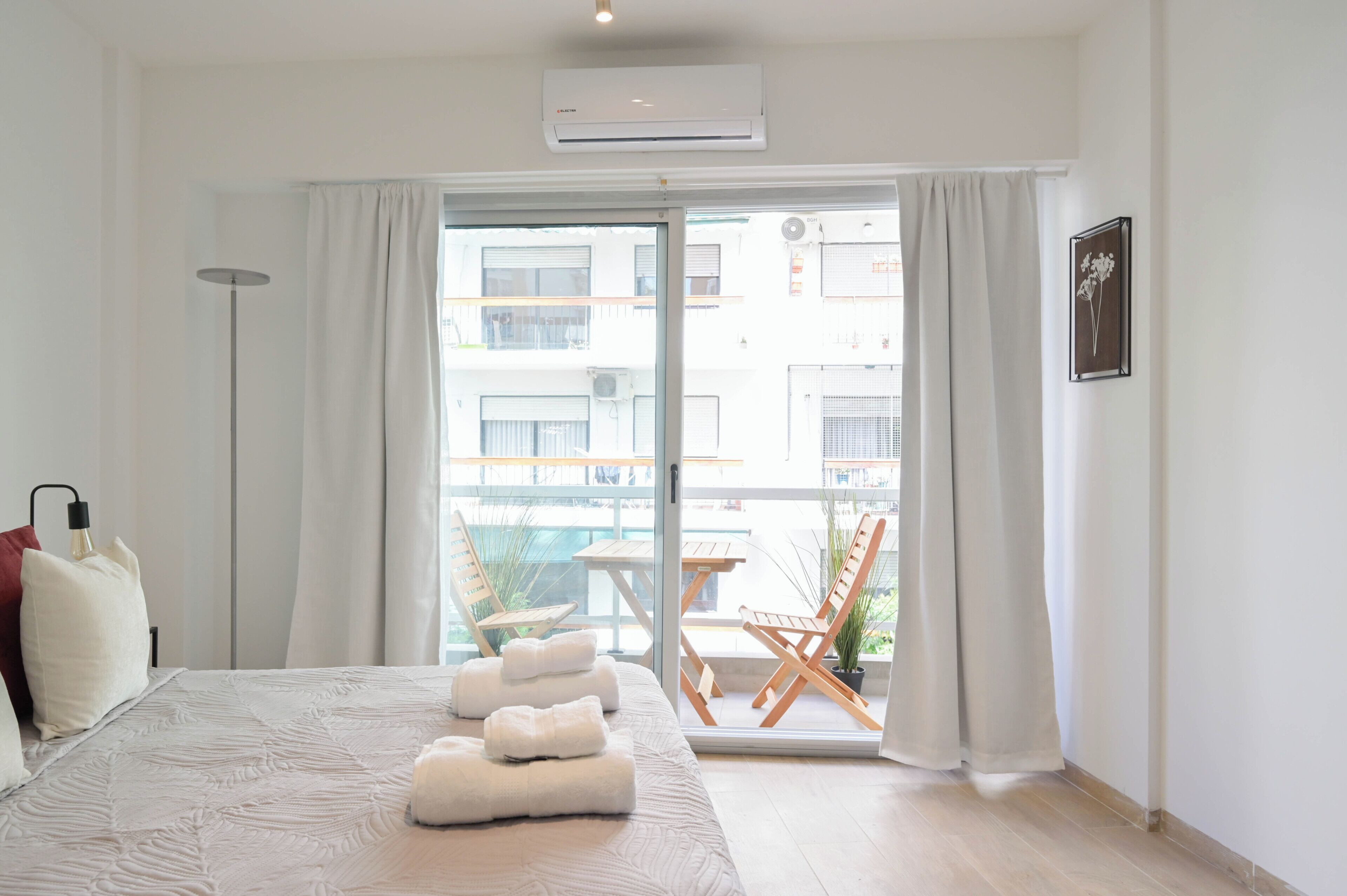 A hotel room with a bed, a bedside lamp, a window with curtains, and a view of the outside balcony.
