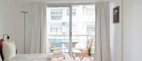 A hotel room with a bed, a bedside lamp, a window with curtains, and a view of the outside balcony.