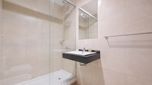 A modern bathroom with a glass shower enclosure, a white bathtub, and a black countertop sink with a mirror above it.