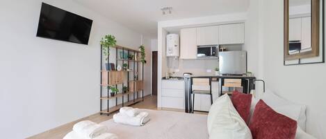 A modern hotel room with a bed, a flat-screen TV, a kitchenette, and a small dining area.