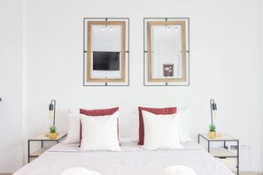 Una habitación de hotel con una cama, dos mesitas de noche, dos espejos fijados a la pared y una pequeña planta en cada mesita de noche.