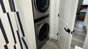 A laundry room with two stacked front-loading washers and dryers, a white door, and a striped curtain.